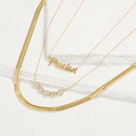 Gold layered necklaces featuring a nameplate pendant and a diamond bar pendant arranged on a white surface.