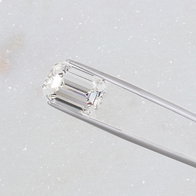 Emerald‑cut loose diamond held by metal tweezers on a light background.