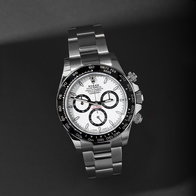 Stainless steel chronograph watch with white dial and black ceramic bezel on a dark background.