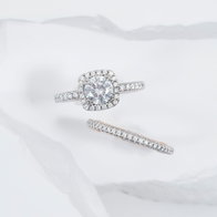White gold cushion‑halo diamond engagement ring with matching diamond band on a white background.