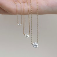 Three solitaire diamond pendant necklaces in graduated sizes displayed on a hand.
