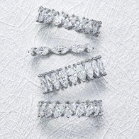 Four marquise‑cut diamond eternity bands in white gold arranged vertically on a textured background.