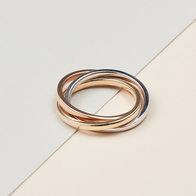 Tri‑color rolling ring with intertwined yellow gold, white gold, and rose gold bands on a neutral background.
