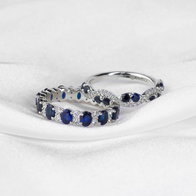 Two white gold bands with blue sapphires and diamond accents displayed on a white fabric background.