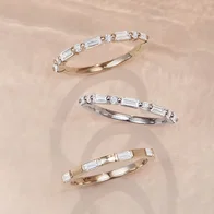 Three diamond baguette stackable bands in yellow gold and white gold arranged on a neutral background.